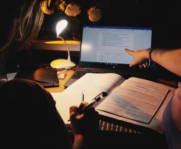 Student using a note-taking app on a laptop beside open textbooks at a desk lamp