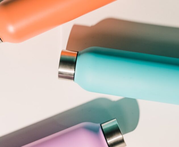 Three insulated stainless steel water bottles in different colors on a white surface