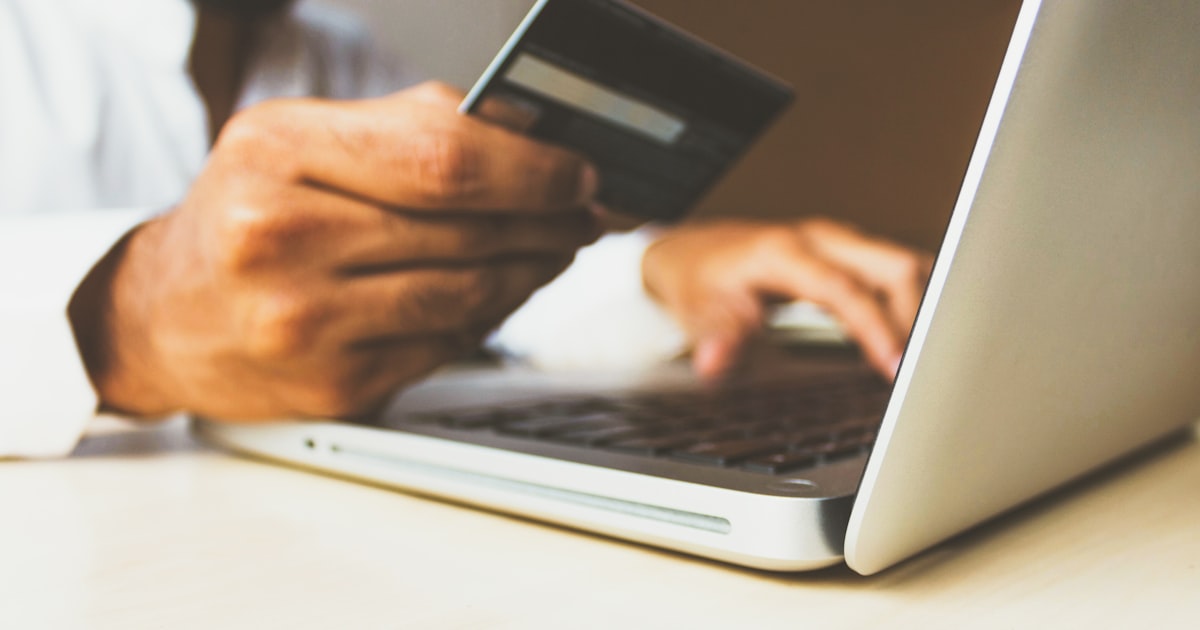 Person entering card details into a laptop while banking online at a desk