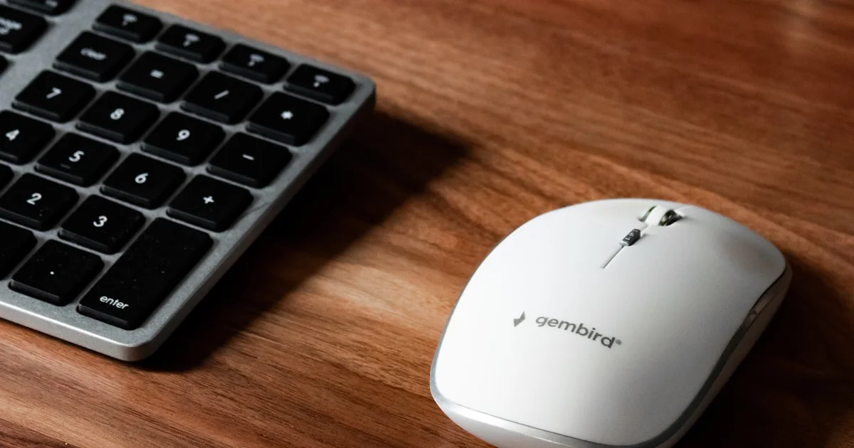 White wireless mouse beside a number pad on a wooden office desk