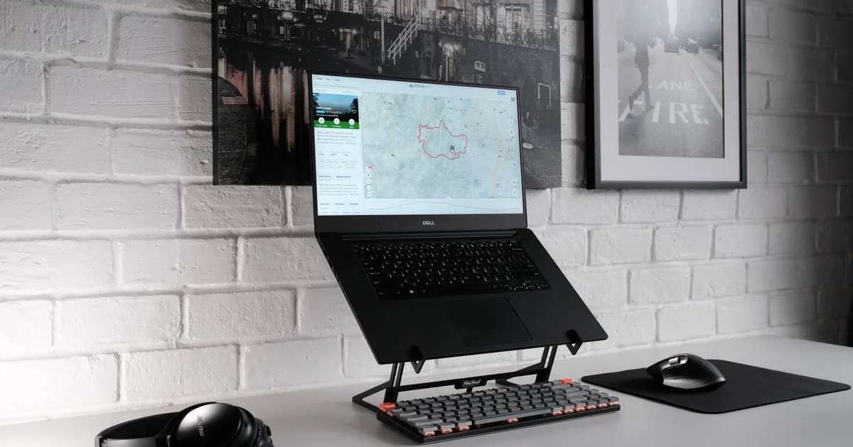 A laptop raised on a black adjustable laptop stand above an external keyboard and mouse on a white desk