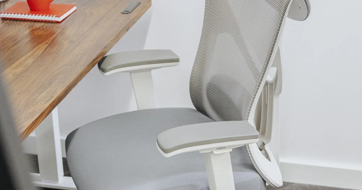 A gray mesh-back task chair with adjustable armrests pulled up to a wooden desk in a home office