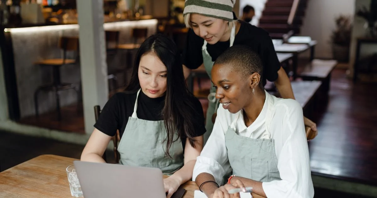 Three small business owners in aprons sharing one laptop in a cafe while choosing the best email client for small business