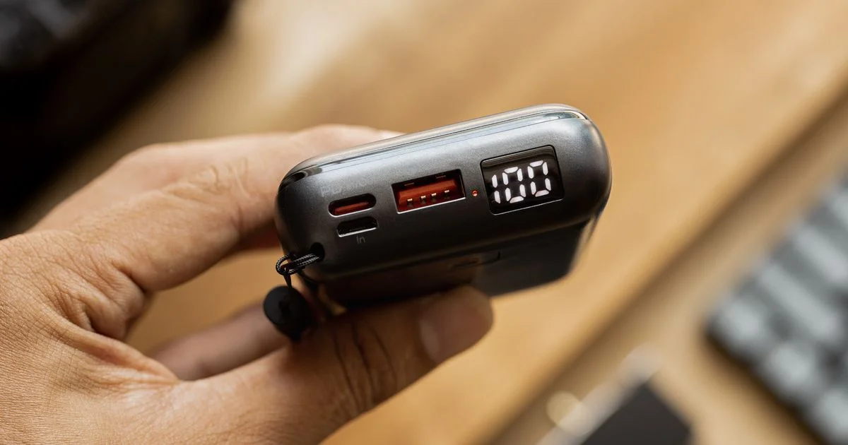 A hand holding the best portable charger for travel, its display showing a full 100 percent charge