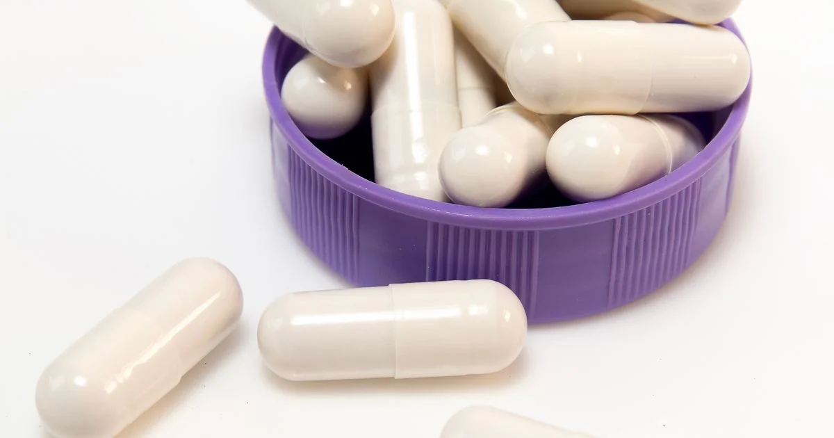 White capsules spilling from a bottle cap, the format used by the best probiotic supplements for gut health
