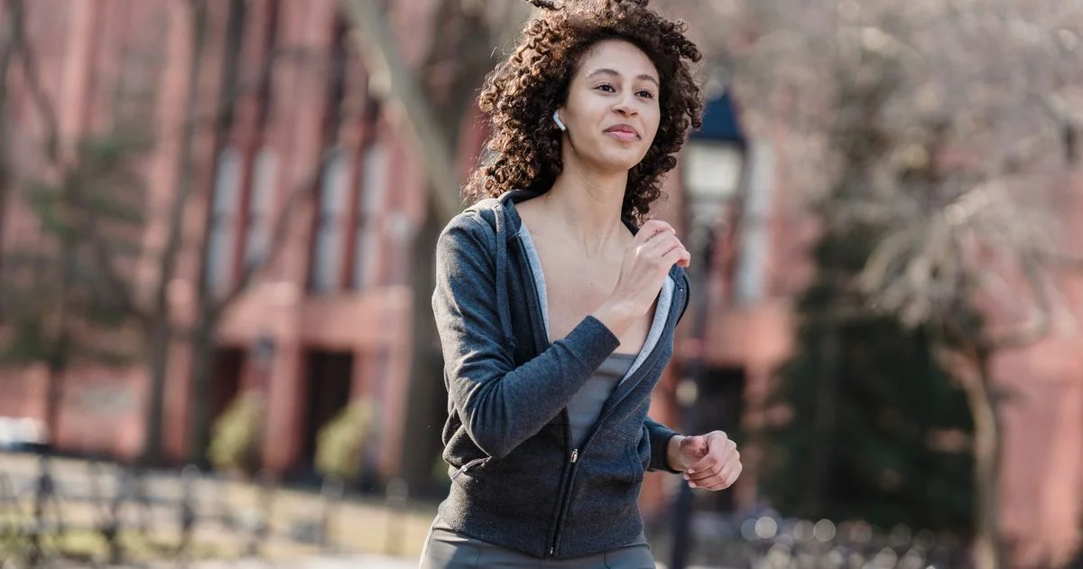 A runner outdoors wearing the best running headphones for marathon training, one wireless earbud visible