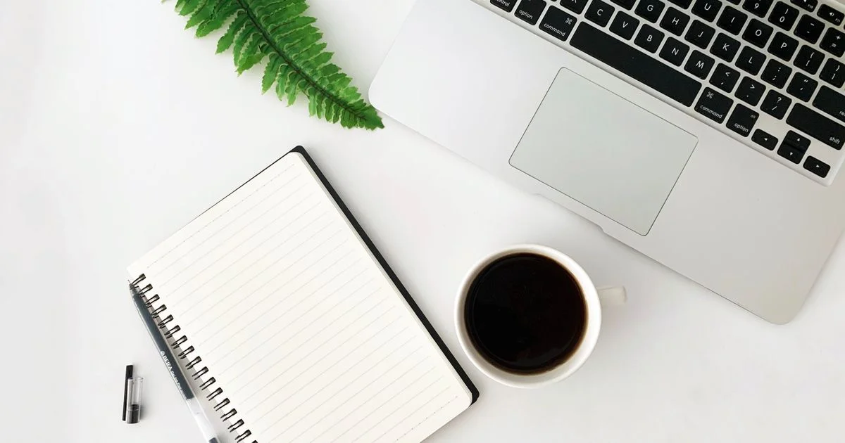 A plain mug of black coffee on a white desk beside a laptop and notebook, the office scene where the best smart mug for coffee lovers is meant to help