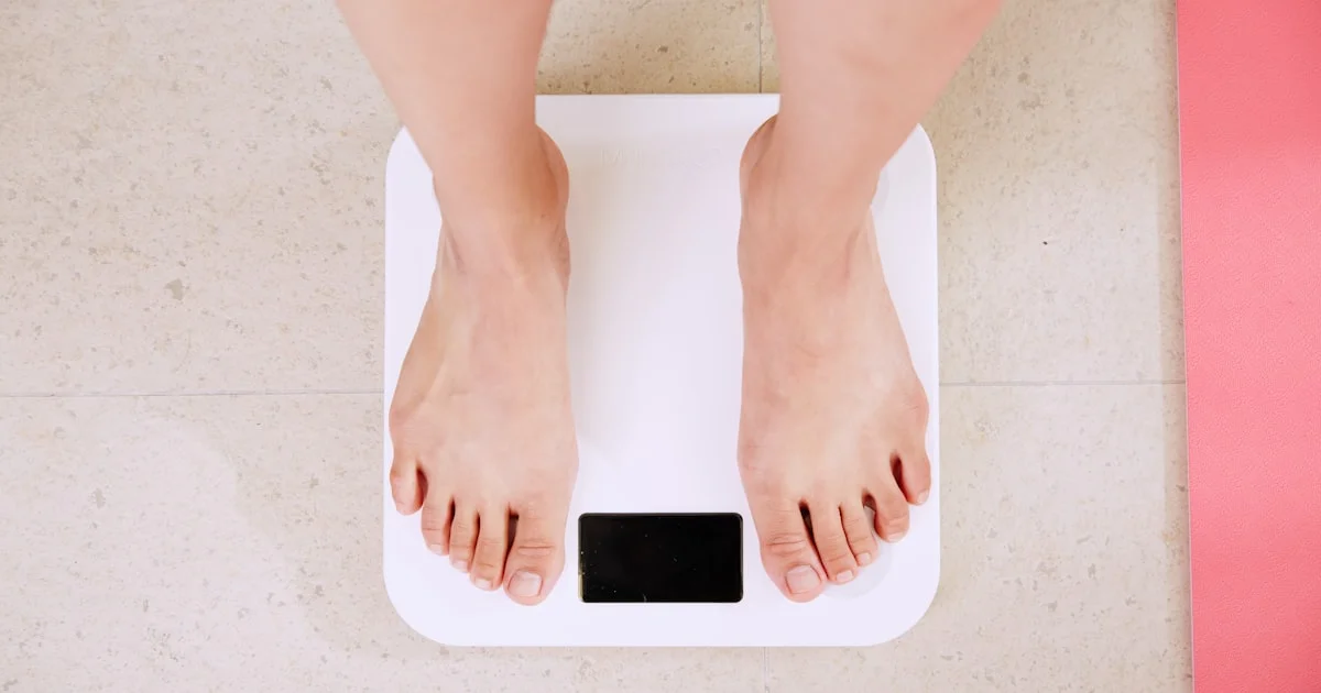 Bare feet standing on a white digital bathroom scale, the contact points a smart scale for body fat uses to measure
