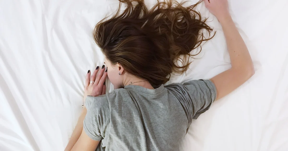 Hot sleeper lying on white sheets with the covers pushed aside, the situation a cooling mattress pad is meant to fix
