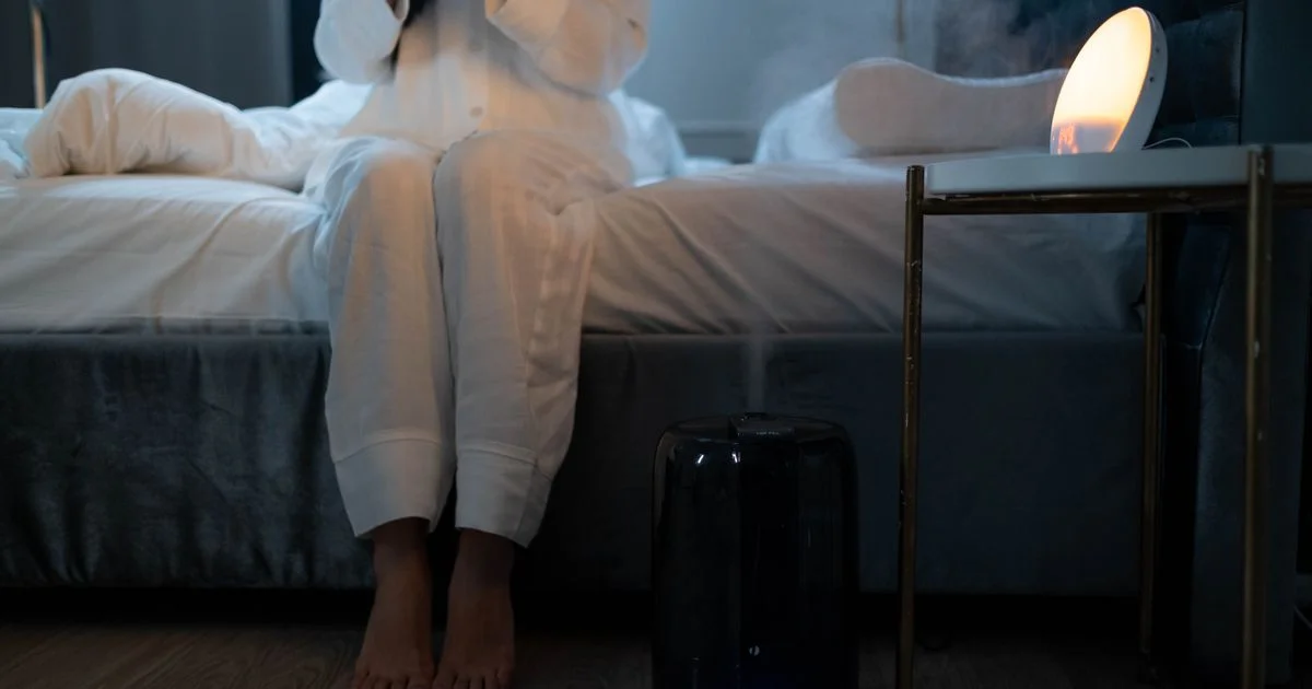 A cool-mist unit running on the floor beside a bed at night with visible mist, the scene a humidifier for bedrooms is bought for