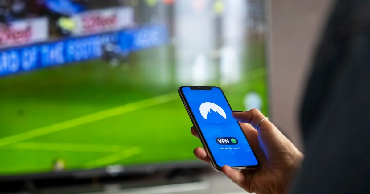 Person holding smartphone with VPN app while sports stream on TV — NordVPN vs Proton VPN use cases