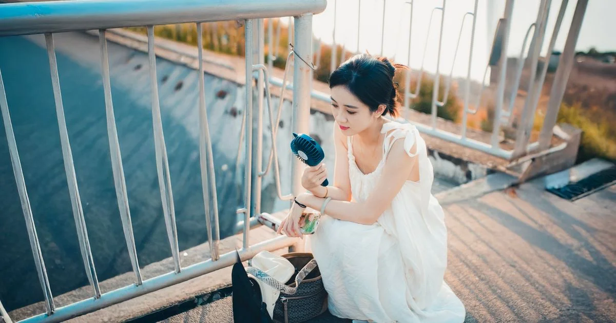 Woman cooling off outdoors in summer heat with a portable fan, the same use case a portable neck fan for summer covers