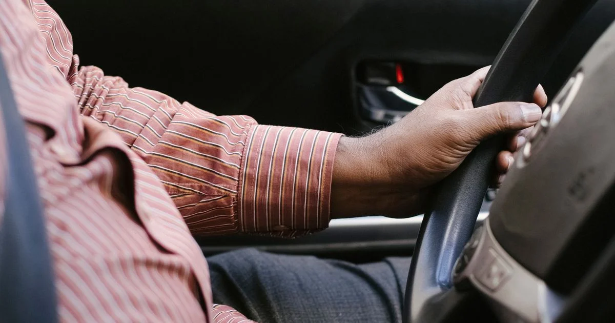 A driver seated with a seat belt on during a long drive, the main use case for a portable seat massager