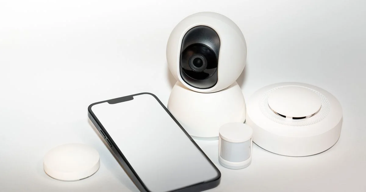 White pan-and-tilt camera beside a phone, the kit behind the best smart camera for Google Home for the front door