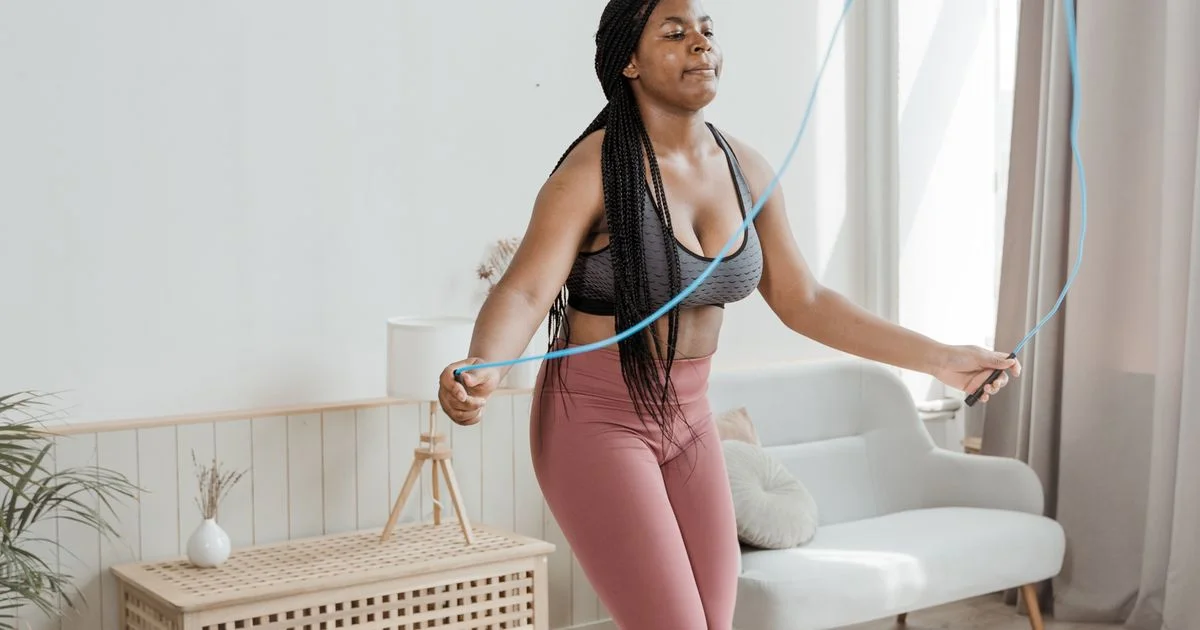 A woman skipping with a plain rope in a bright living room beside a sofa, the kind of space a smart jump rope for home workouts has to fit into