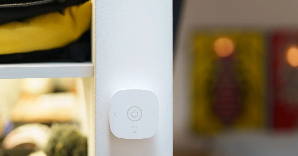 A white wall-mounted control with a power button and a lamp icon, the kind of smart light switch for the living room that replaces an existing wall switch