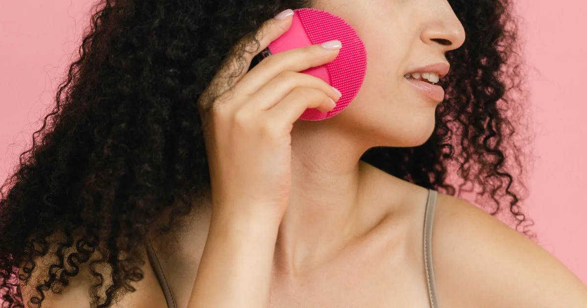 A woman using a silicone sonic facial cleansing brush along her cheek during a skincare routine