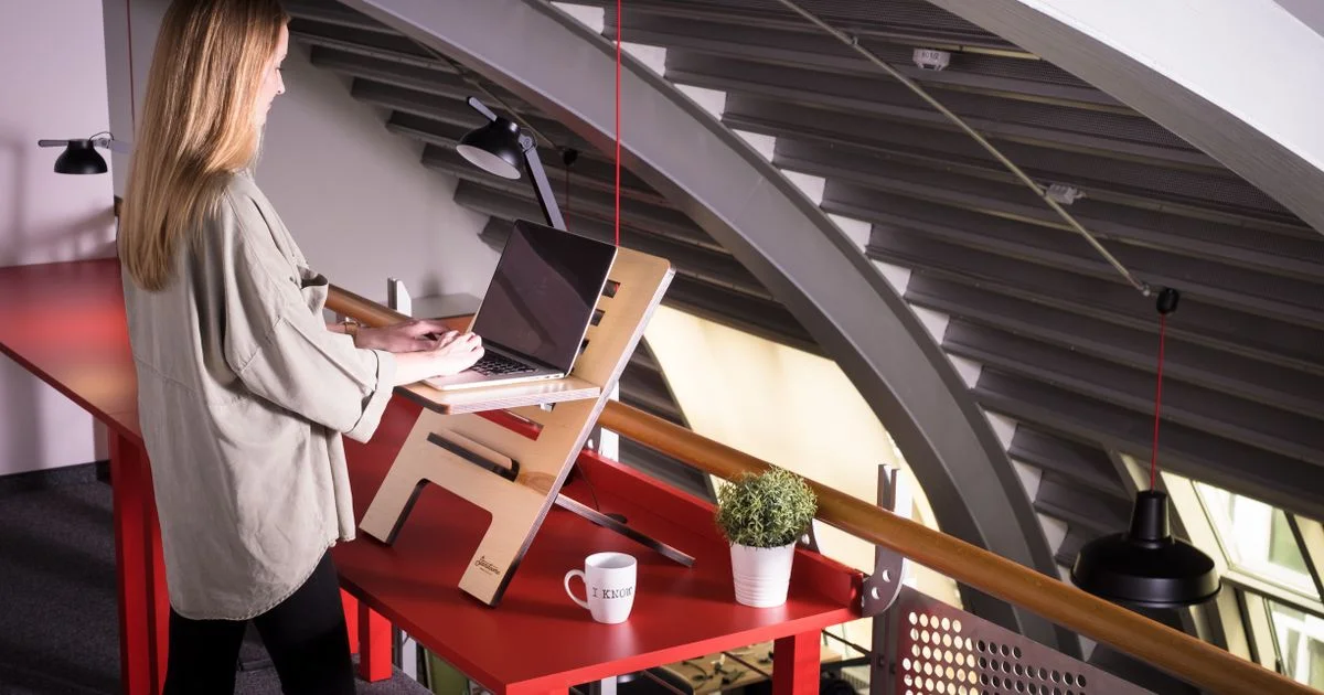 Woman using a laptop on a standing desk converter set on top of an existing desk at home