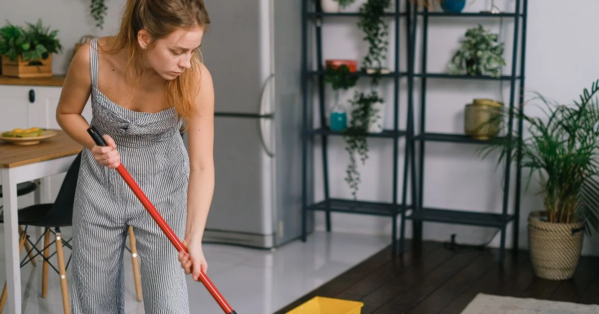 A woman mopping a kitchen where pale tile meets dark wood, the split that decides whether a steam mop for hardwood floors is safe