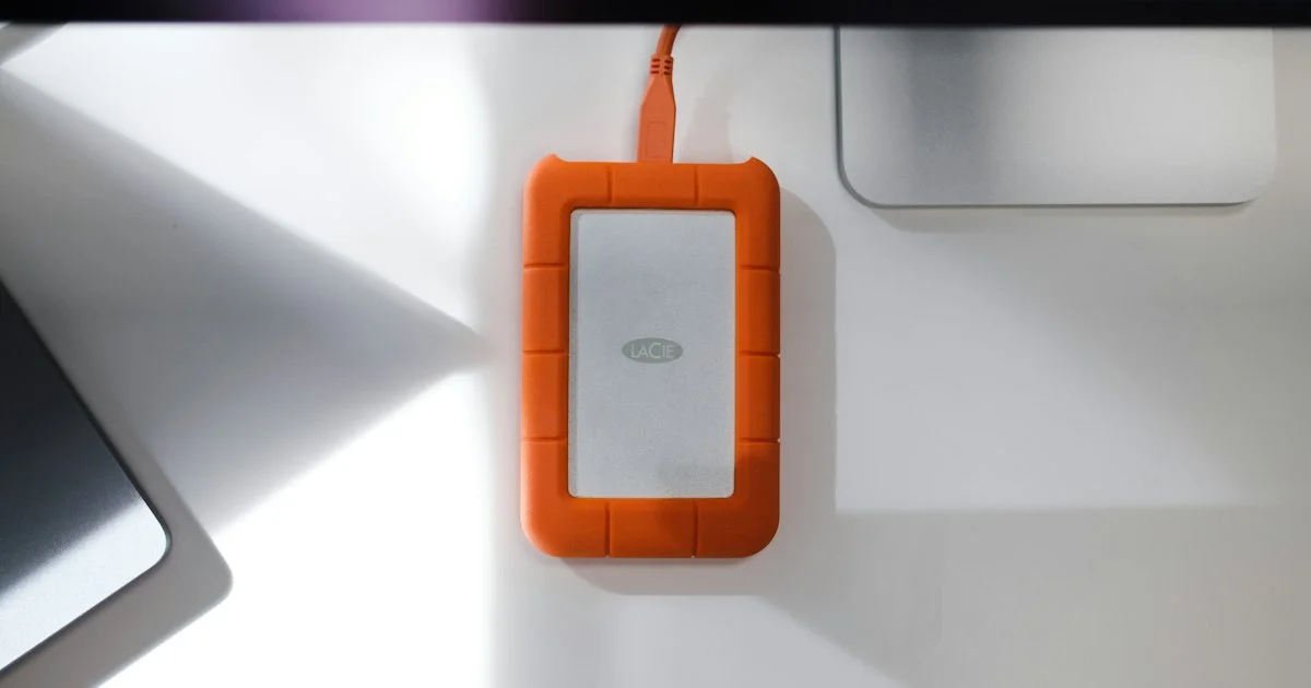 Rugged orange portable external hard drive for backup sitting on a white desk next to a computer