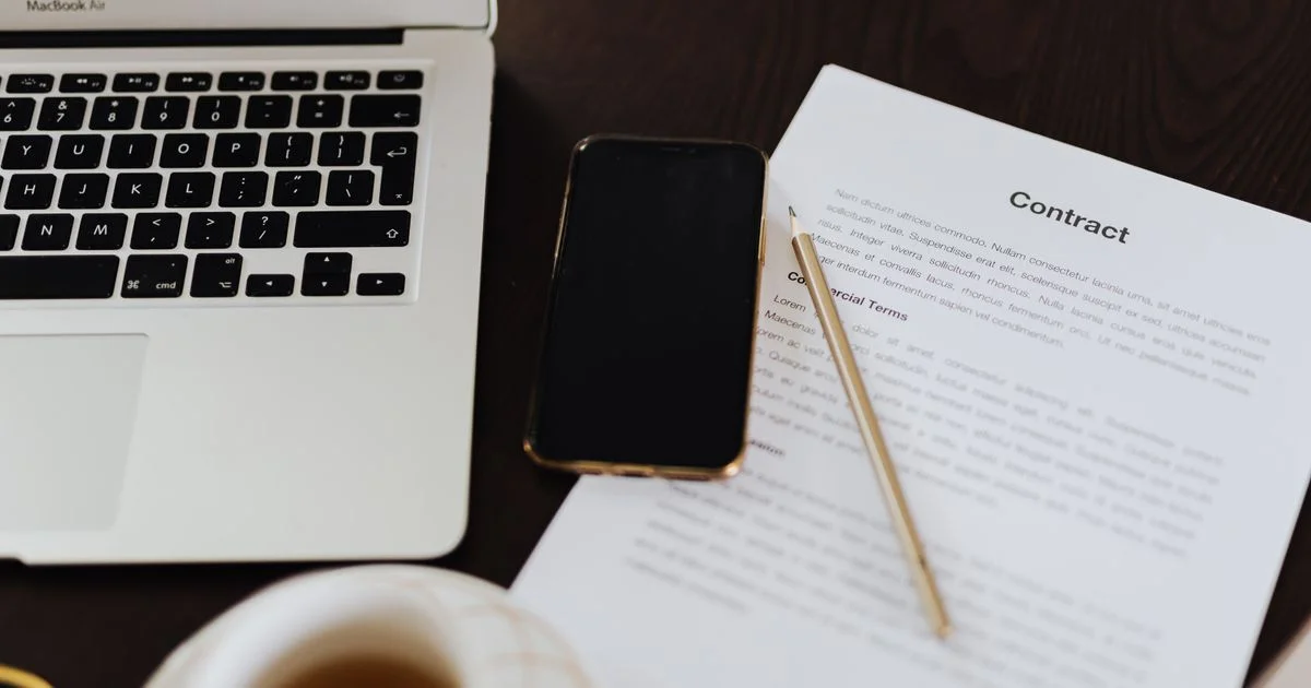 A contract document, pen, phone and laptop on a desk, the kind of paperwork a PDF editor app handles