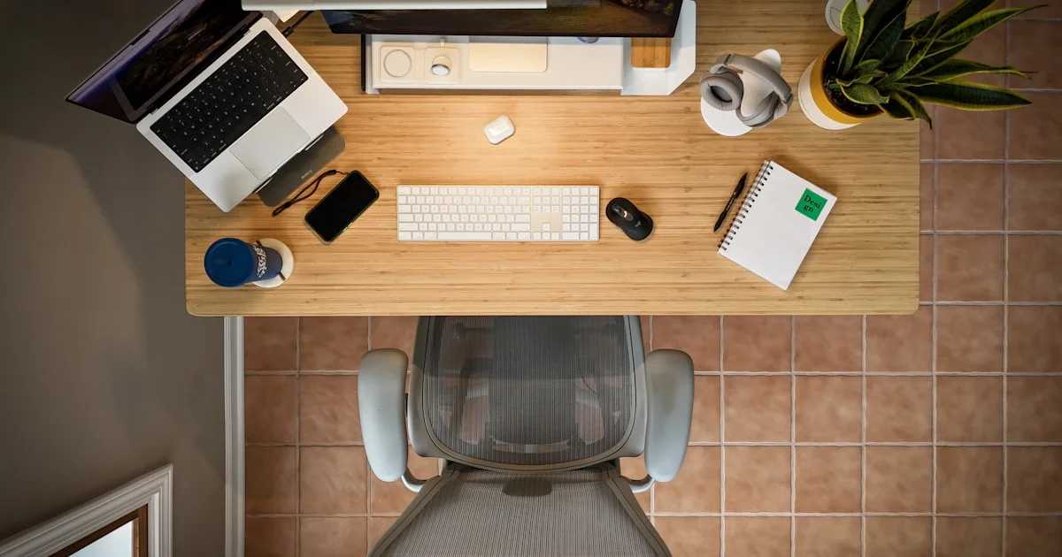 Overhead view of a tidy desk with a laptop stand, external keyboard, mouse, notebook and headphone stand