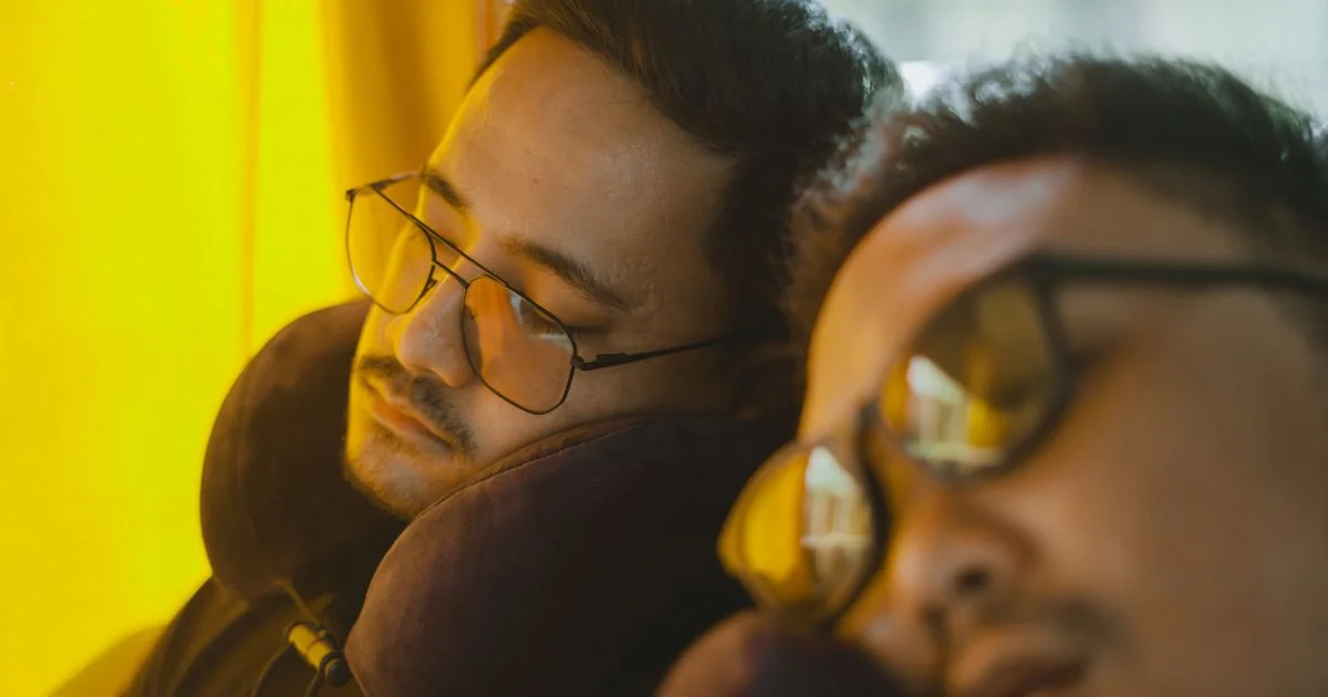 Two travelers asleep in their seats wearing neck pillows, the situation a travel neck pillow with speaker for long flights is built for