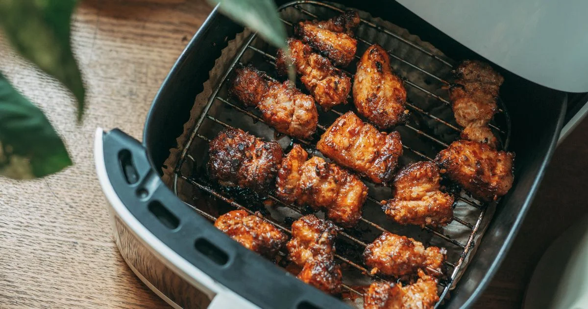 Seasoned chicken pieces browned on the rack of an unbranded air fryer basket on a wooden counter, the everyday job a Walmart air fryer for small kitchens is bought to do