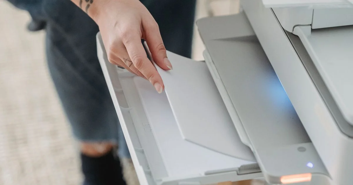 A hand loading plain paper into the tray of a white desktop machine, the routine that decides whether a budget printer for the home office earns its place