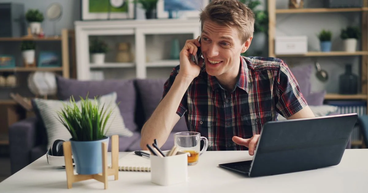 Man taking a call at a home desk beside an open laptop, the everyday setting for a dedicated IP VPN for remote work