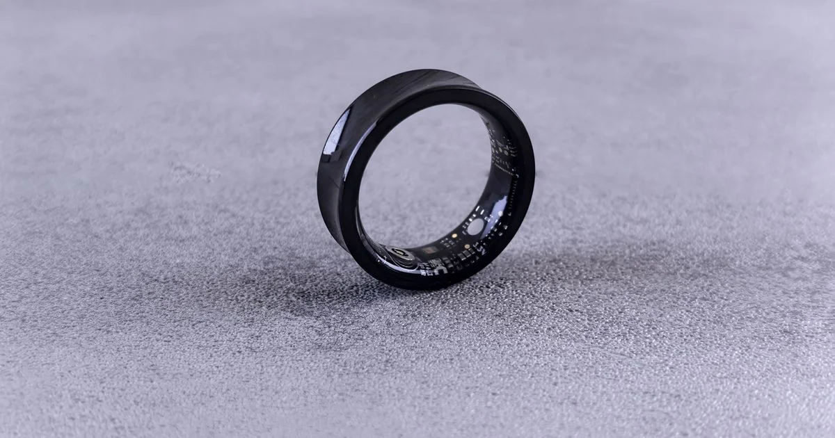 A black sensor ring resting on a grey surface with its inner optical array visible, the shape an invisible health tracker for daily wear usually takes