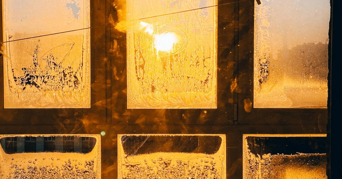 Frost-covered window panes lit by a low winter sunrise, the dark morning a light therapy lamp for seasonal depression is meant to answer