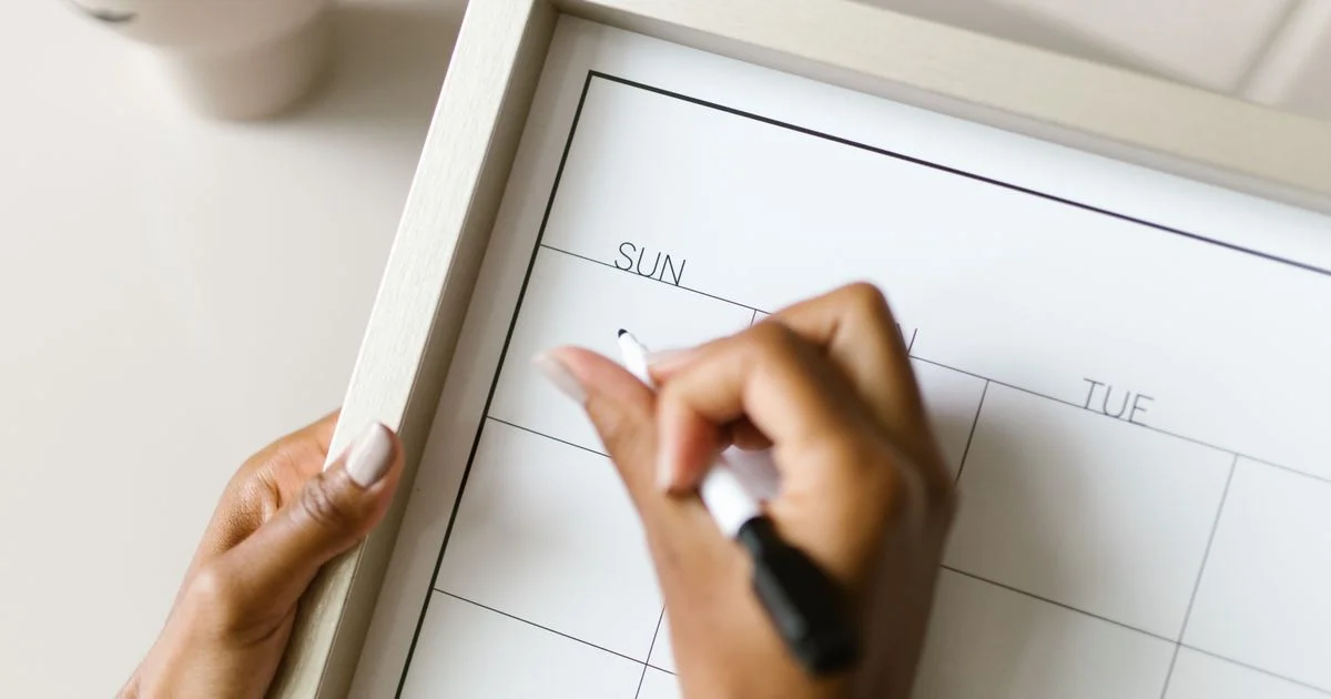 Hand marking a blank weekly planner board, the kind of schedule a best red light therapy device for home use has to fit into